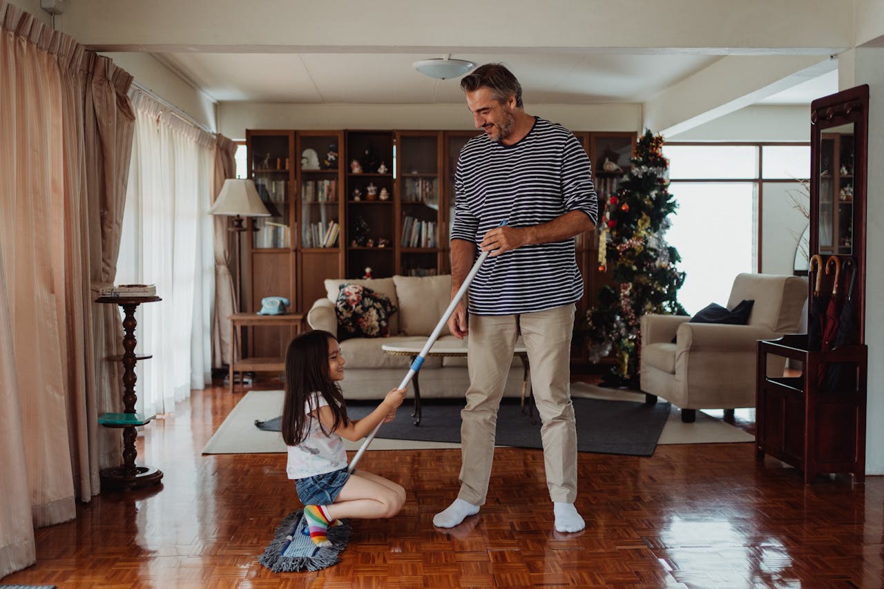 portfolio-01 Father and daughter happily cleaning and bonding at home, surrounded by a cozy living room setting.