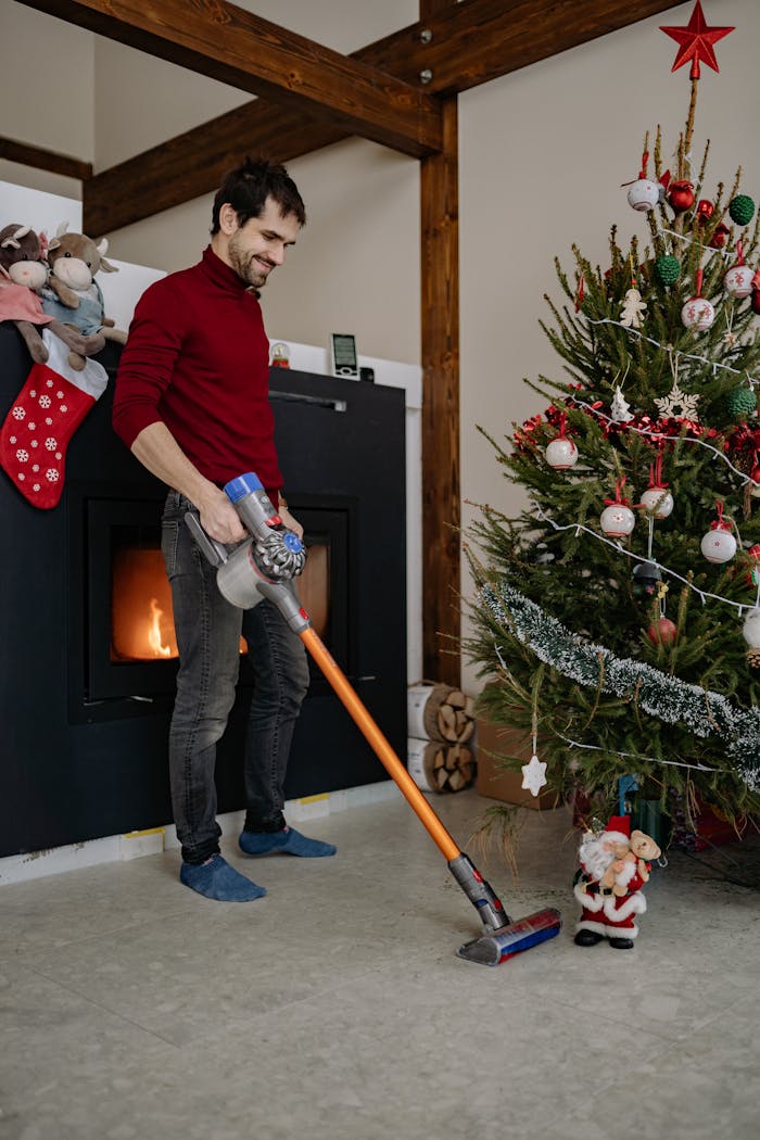 portfolio-04 A man vacuuming the floor beside a decorated Christmas tree with holiday decor and a fireplace.